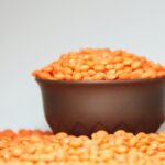 A focused image of a bowl filled with vibrant red lentils against a plain background.