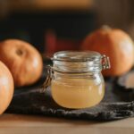 A cozy still life with homemade apple cider in a glass jar surrounded by pumpkins on a wooden table.