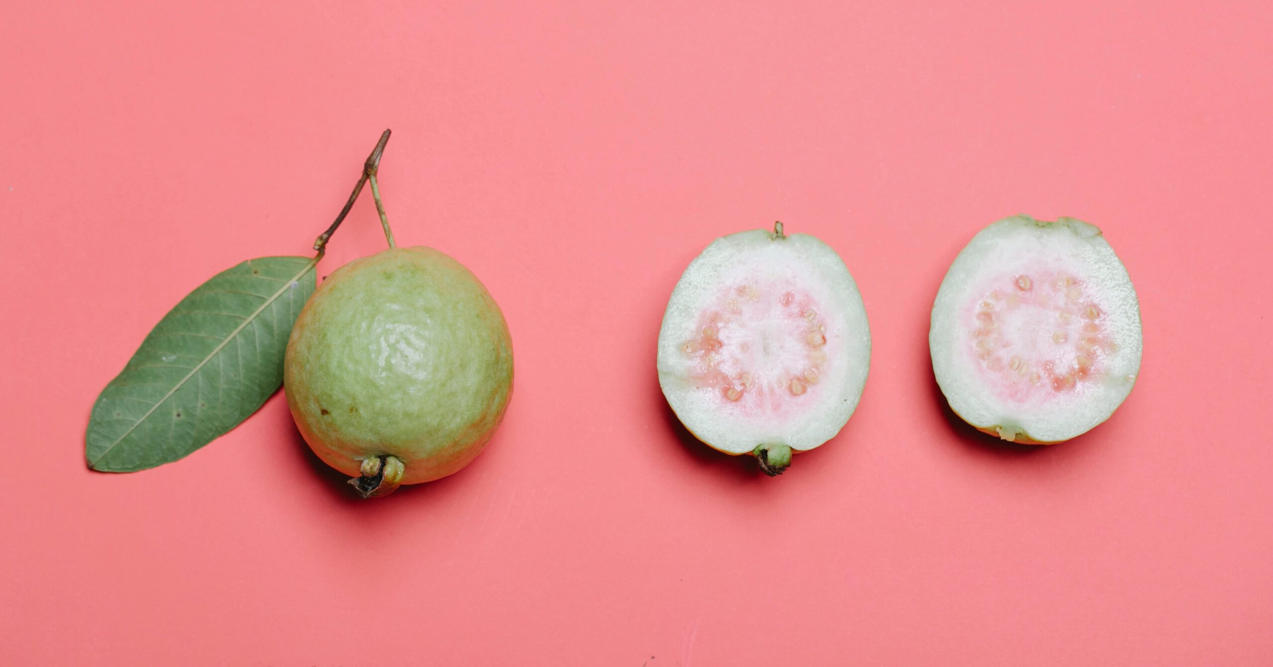 Whole and cut guava with leaf on pink background. Perfect for healthy eating concepts.