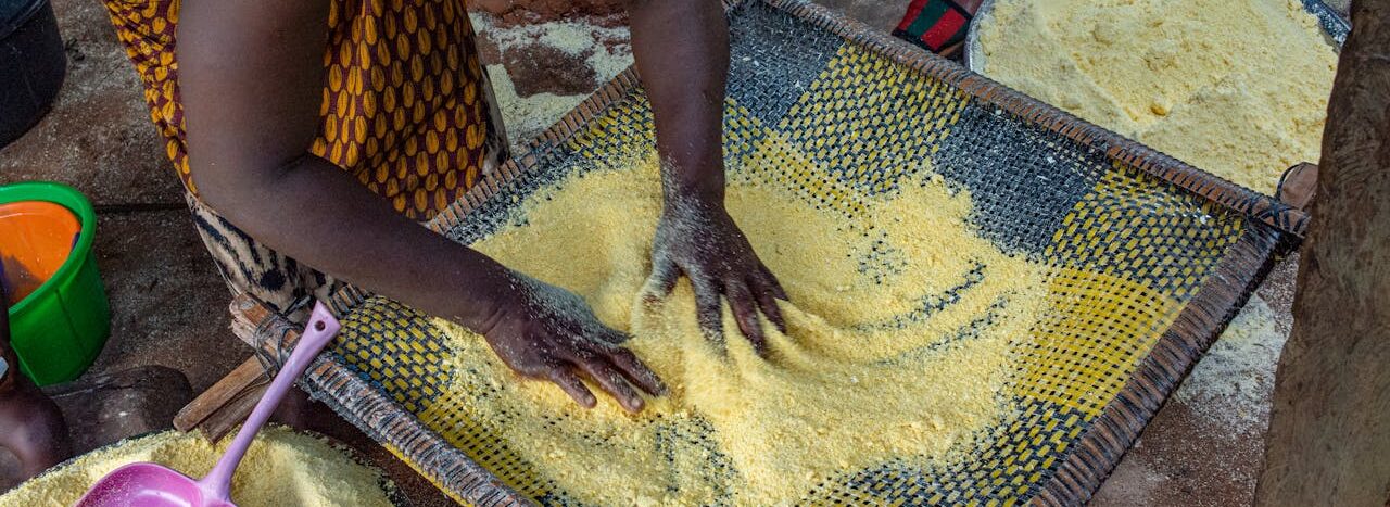 A woman works with a sieve to prepare traditional African maize meal outdoors.
